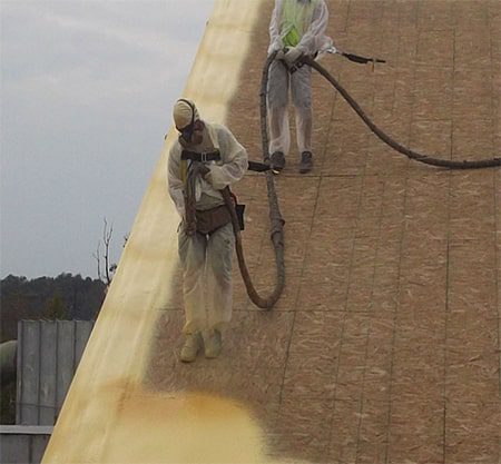 roofers tied off on a sloped roof installing spray foam