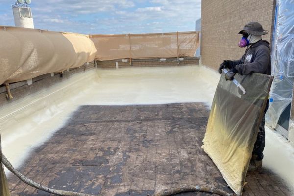 A spray foam installer holding a guard to prevent overspray